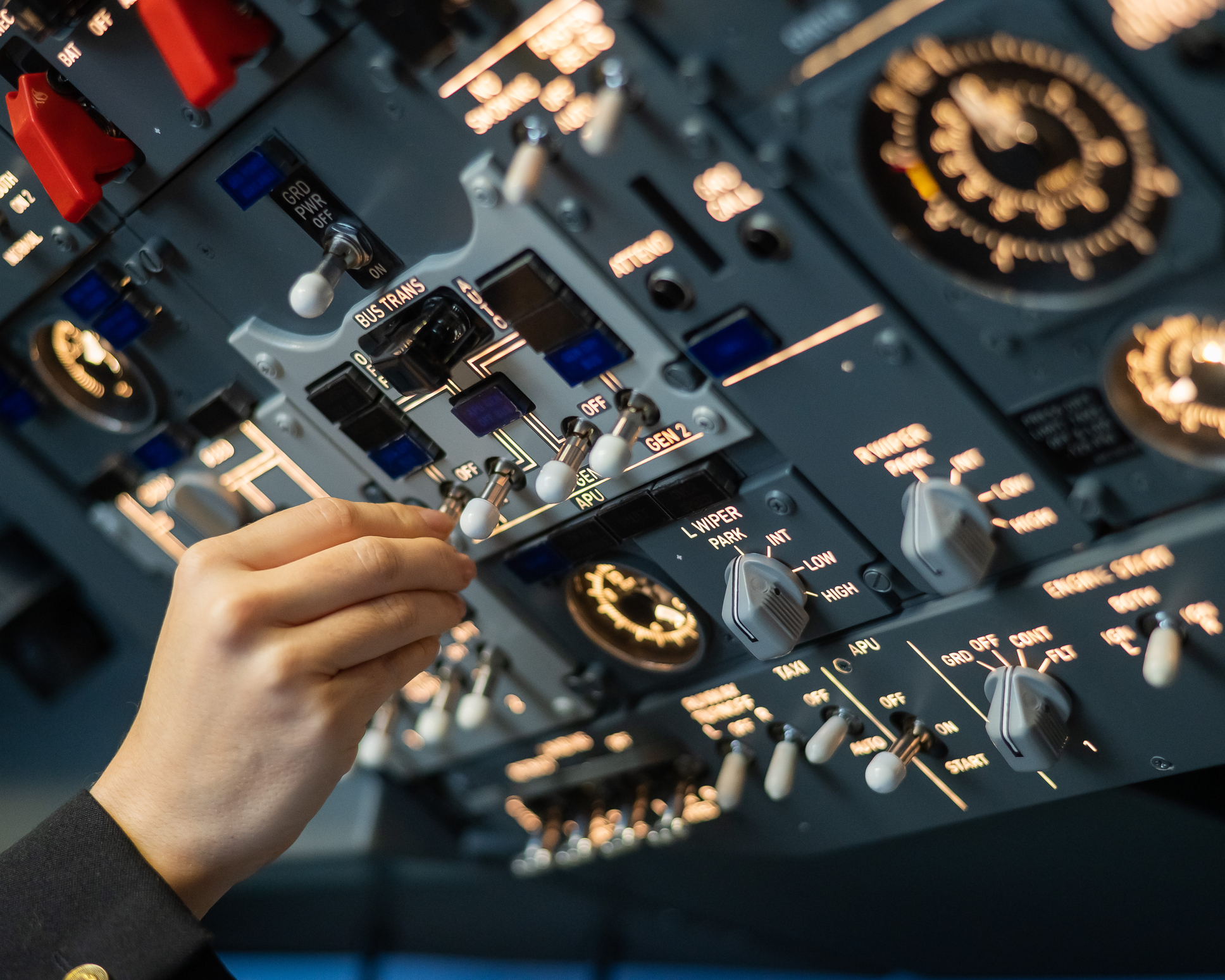 A hand operates a small switch on a large control panel with numerous gauges and levers in the cockpit.