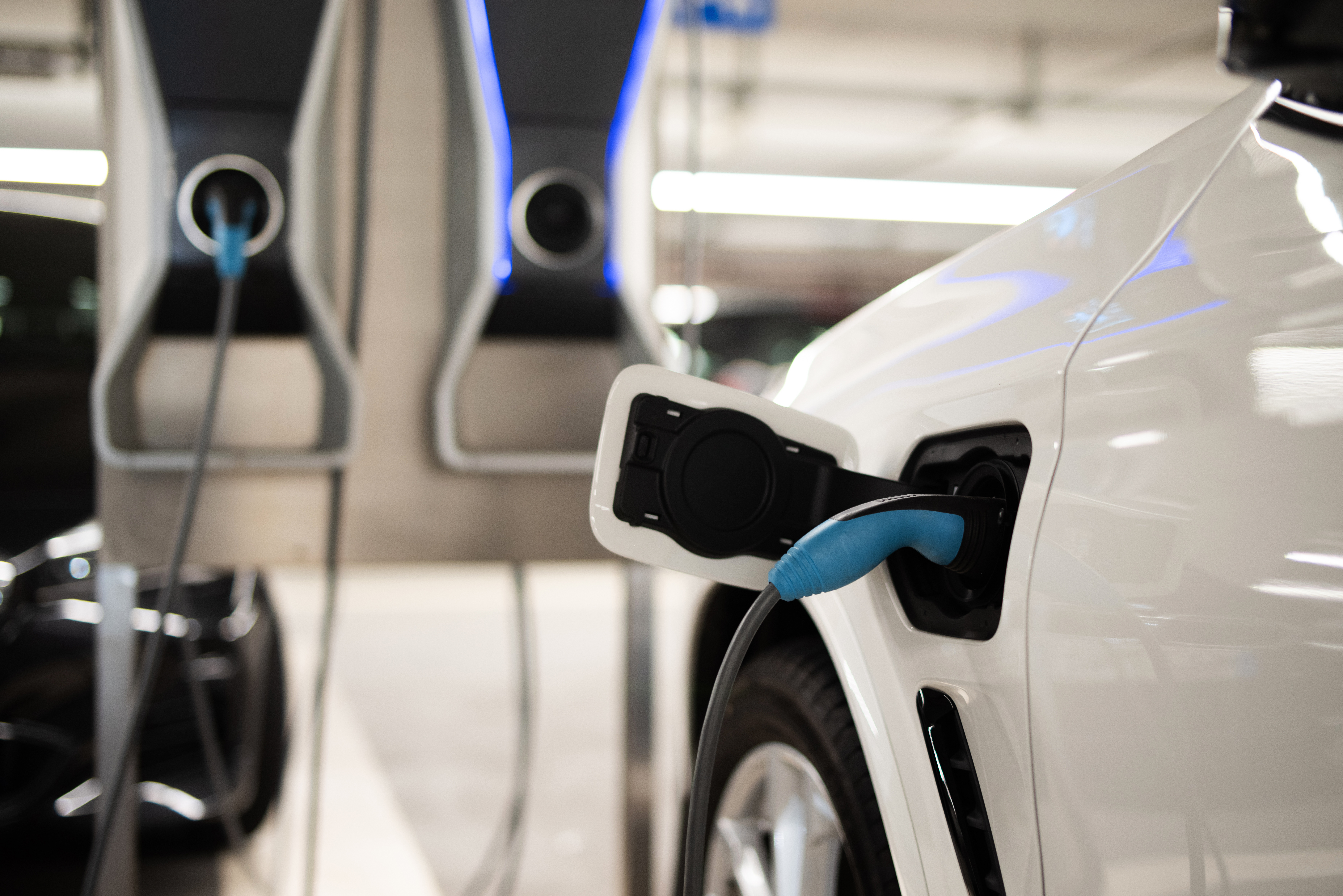 In the foreground you can see the tank opening of an electric car with a charging cable connected, in the background the corresponding charging station.