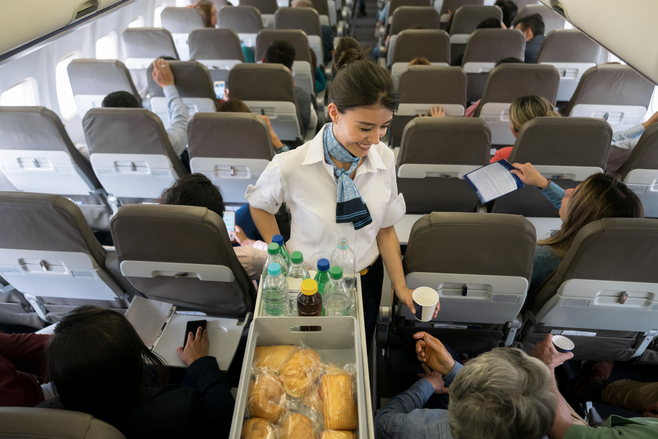 A smiling flight attendant hands a drink to a passenger.