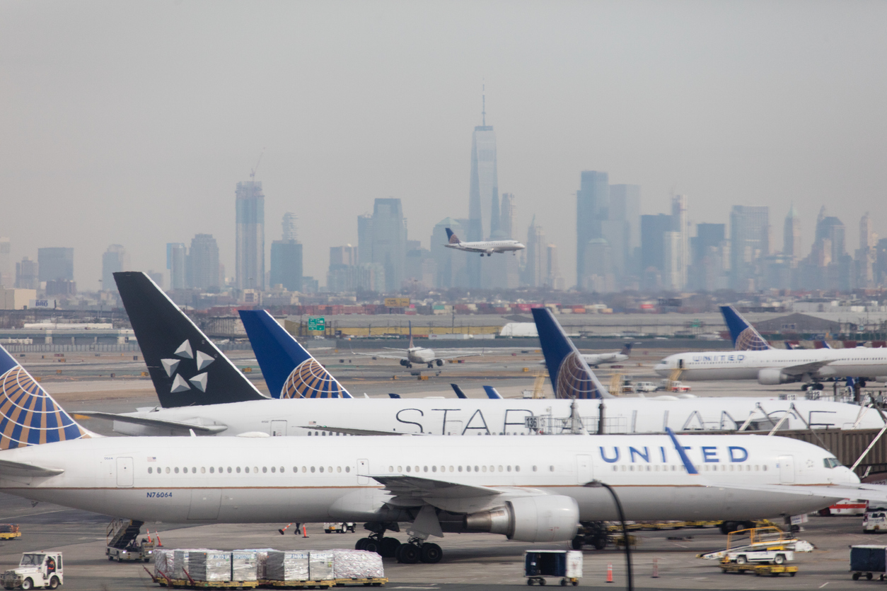 A tarmac with a plane landing and the Manhattan skyline in the background.