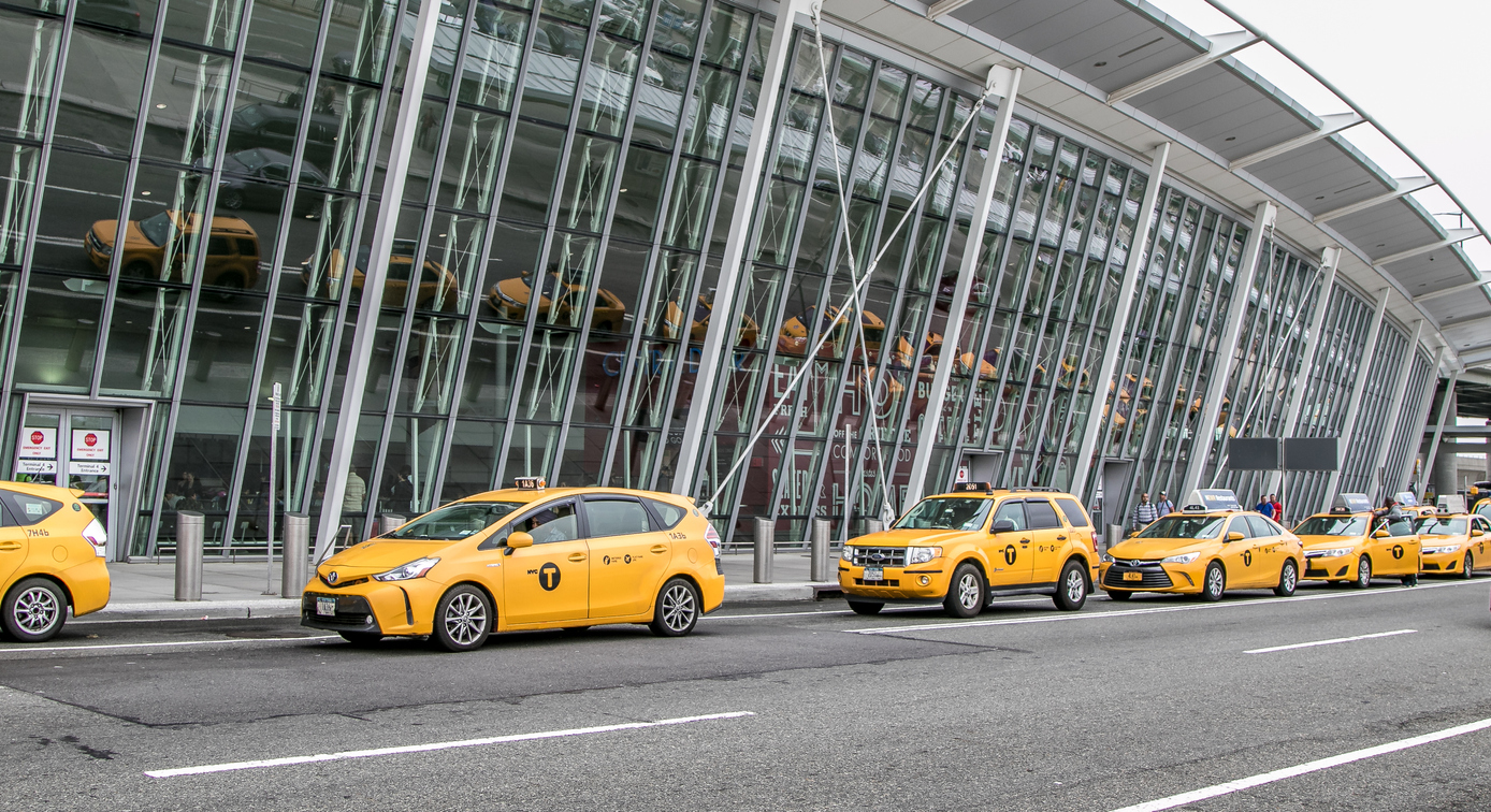 Several parked Yellow Cabs lined up outside a New York airport.