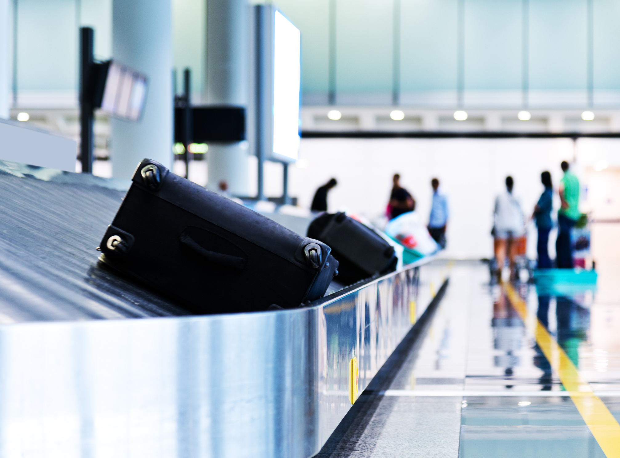 airport baggage carousel with two black suitcases in foreground and several people waiting in background