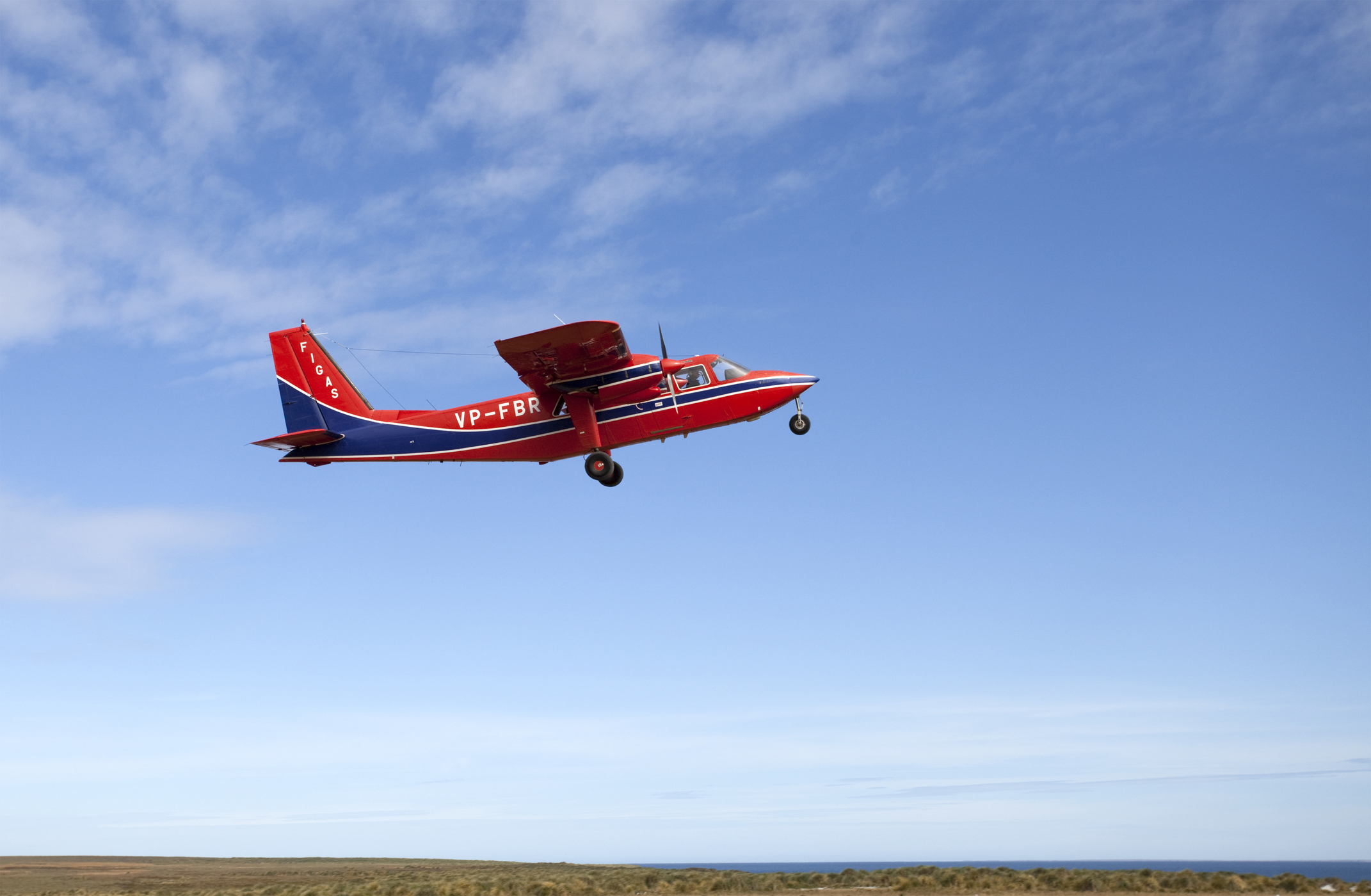A red and blue propeller plane takes off in good weather.