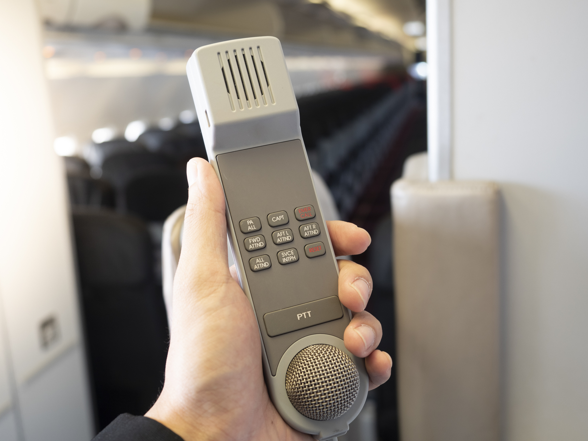 Male flight attendant holding in his hand an intercom in the airplane cabin.