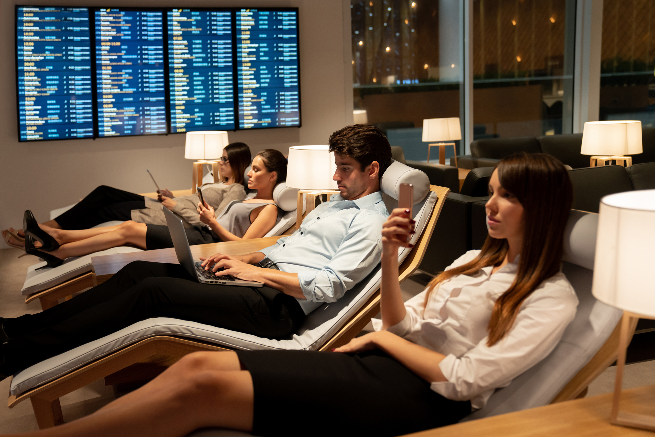 smartly dressed business travelers relaxing in a VIP lounge at the airport and being on their cell phones or laptops while waiting for their flight