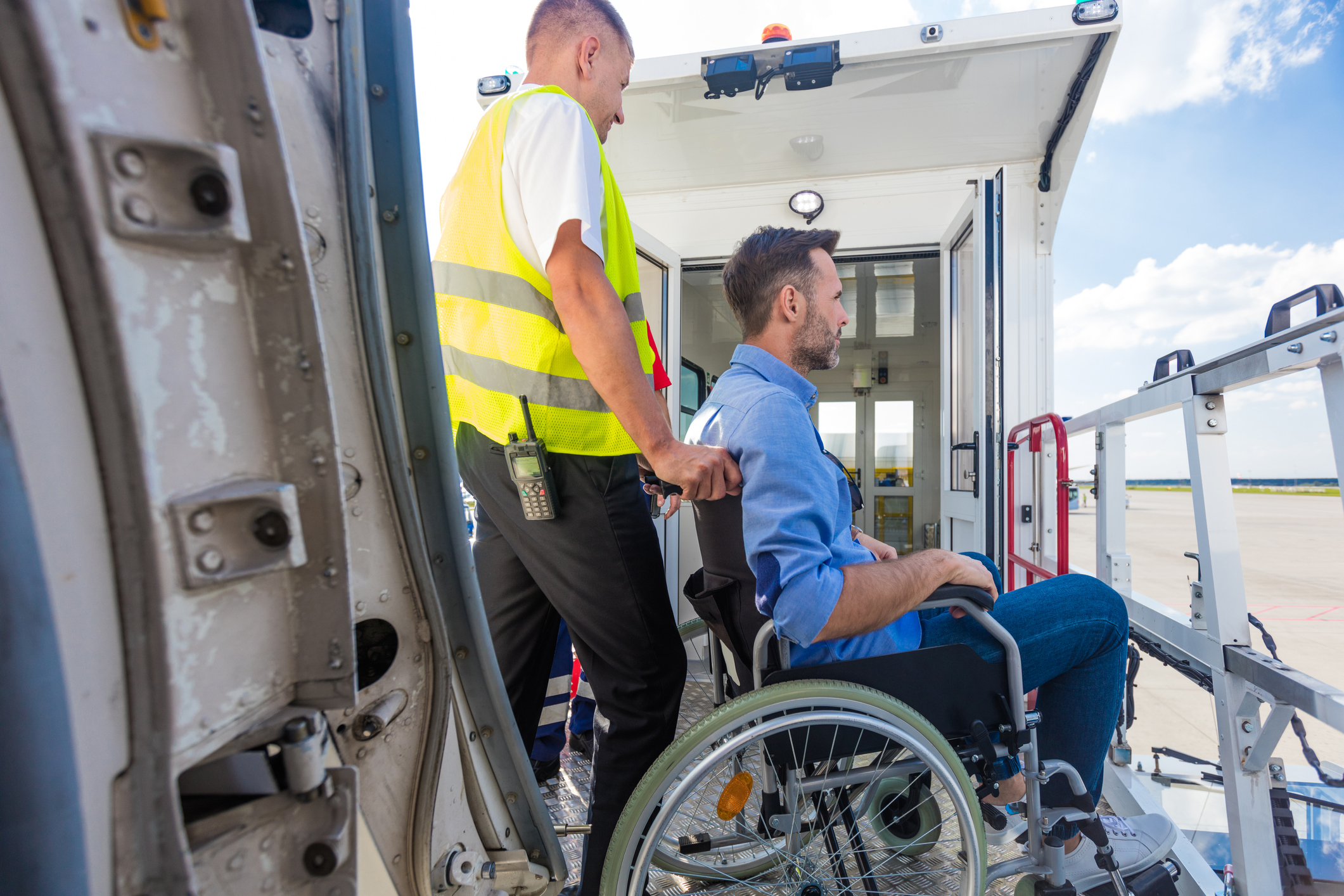 A man in a wheelchair is being pushed by an airline employee; the aircraft door can be seen in the foreground and the gangway in the background.