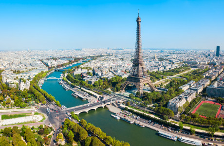 An aerial view of Paris, in the foreground you can see the Eiffel Tower and the Seine River, in the background the city stretches.