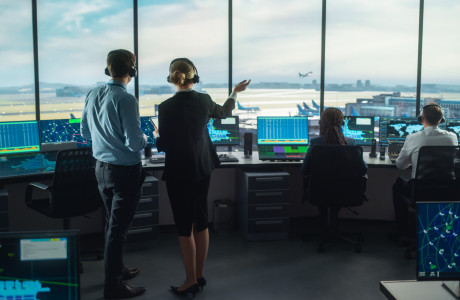 In an airport tower, several people watch an airplane take off.