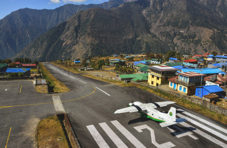 The runway in Lukla in good weather, a propeller plane is just starting its takeoff.