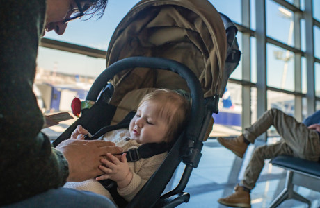 A man sits at an airport terminal and plays with a baby in a baby carriage.