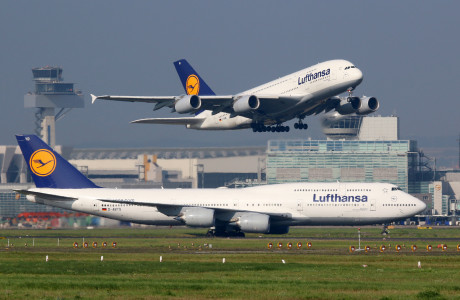 In the foreground a Lufthansa aircraft is on the runway of an airport, in the background a second one is just taking off.