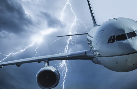 An airplane flies through a thundercloud, lightning flashes in the background.