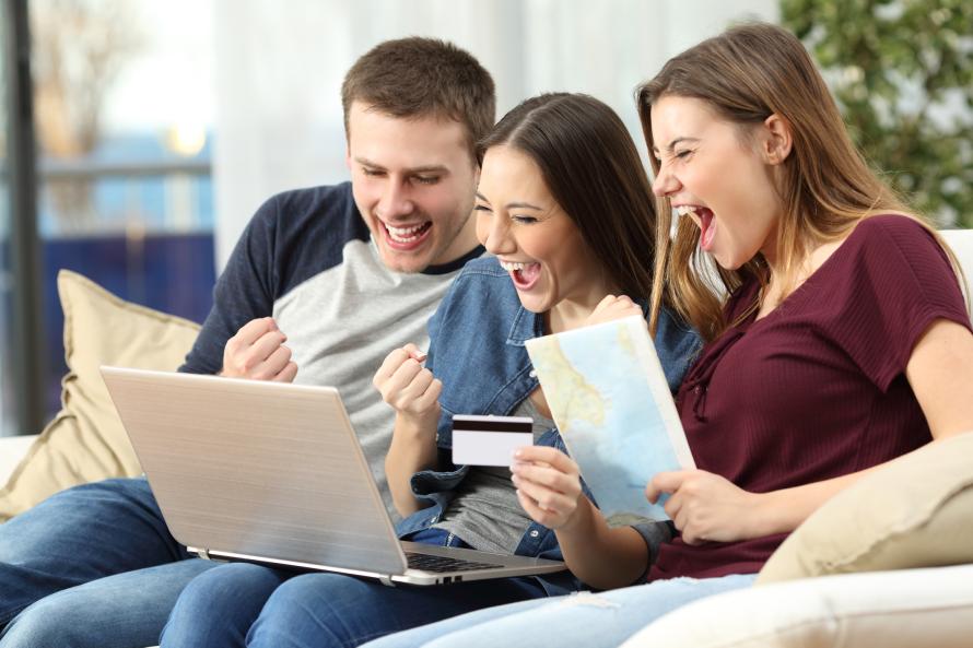 Three young people are cheering while sitting in front of a laptop